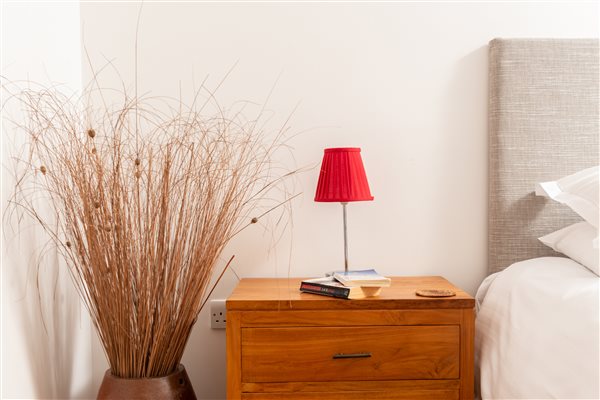 Threshing Barn bedside table with lamp, books and dried grasses standing in large vase on floor